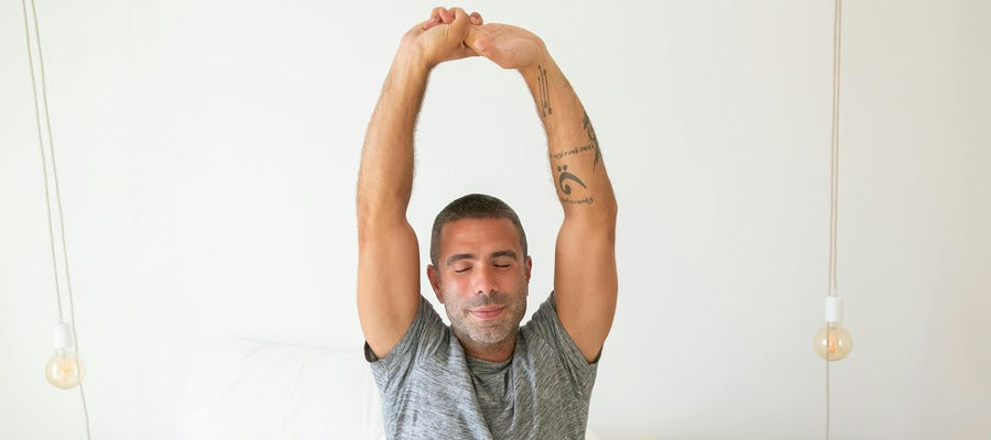 man stretching his arms in bed in the morning after a good night's sleep