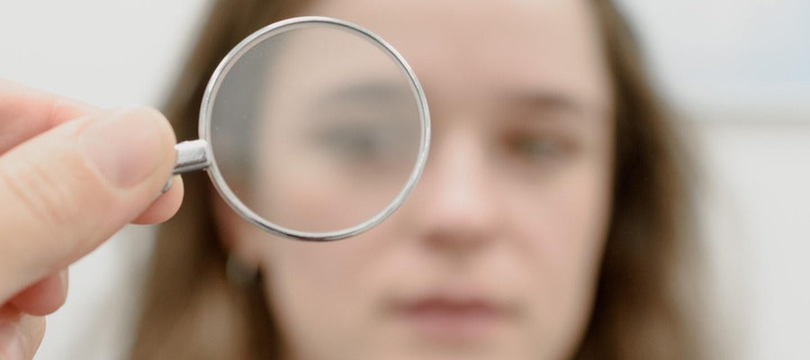 imagen borrosa de una mano sosteniendo una lente sobre el rostro de una mujer en el fondo