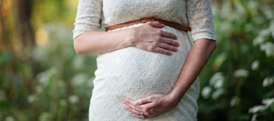 Mujer embarazada con vestido blanco cogidos de la mano sobre su vientre.