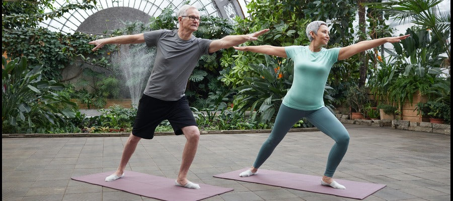 older man and woman doing yoga on mats against leafy green background