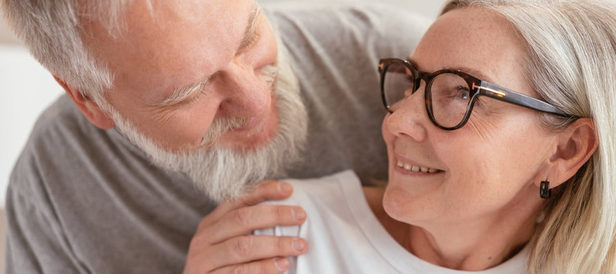 senior white-haired and bearded man touching senior woman's shoulder as she looks at him and smiles