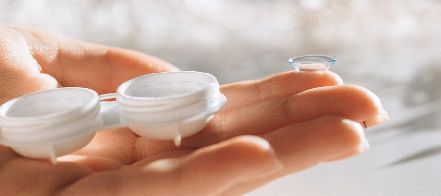 closeup of female hand holding contact lens on the tip of her finger and contact lens case in her palm