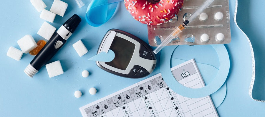 glucose monitor, diabetes medicines and calendar, sugar cubes, and red donut scattered on the table
