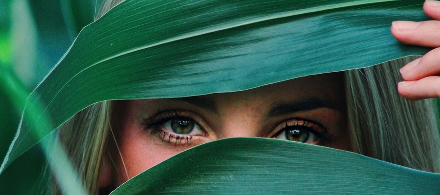 mujer escondiendo su rostro detrás de grandes hojas verdes