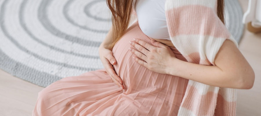 Primer plano de una mujer embarazada sentada con falda rosa tocándose el vientre con ambas manos
