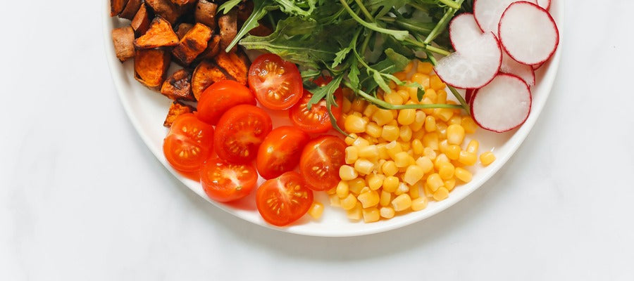 half of a white plate with leafy greens, sliced radishes and cherry tomatoes, corn, and fried vegetables