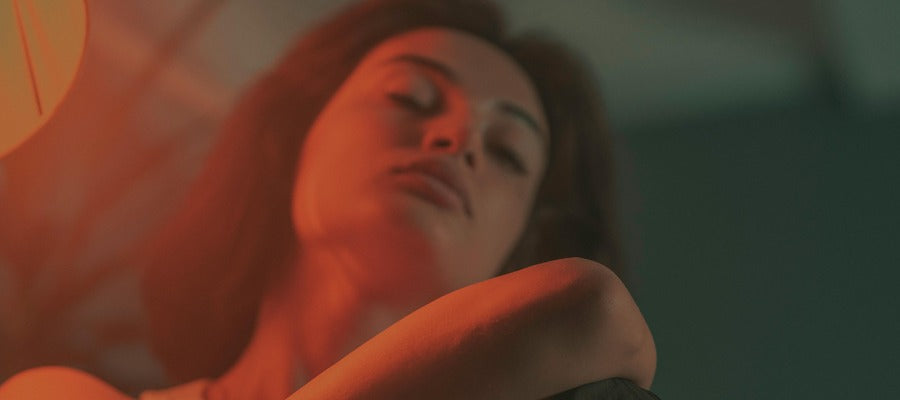 woman with dry eyes keeping her eyes closed to rest them in the red light of a lamp her face seen from below