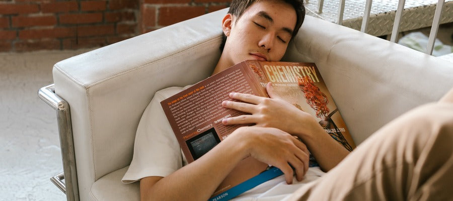 teenage boy napping on couch while embracing large chemistry book