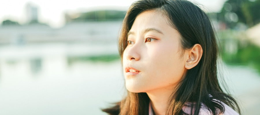 woman looking up with face in the sun against blurry lake background