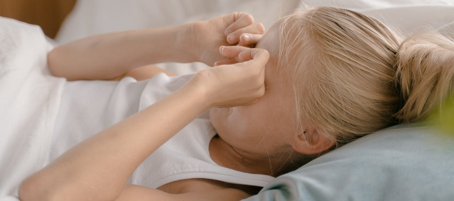 Mujer con cabello rubio y camisa blanca frotándose los ojos después de despertarse.