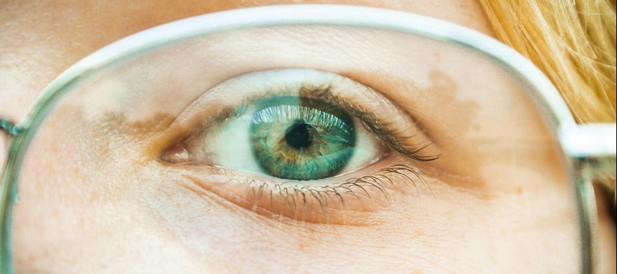 Primer plano de los ojos verdes brillantes y el cabello rojo claro de una mujer vistos a través de la lente con montura plateada de sus anteojos