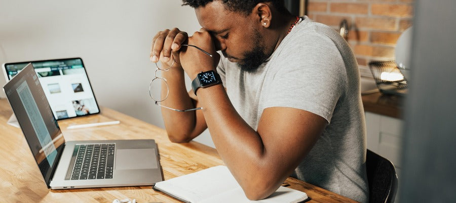 hombre sentado en un escritorio frotándose los ojos después de haberse quitado los anteojos