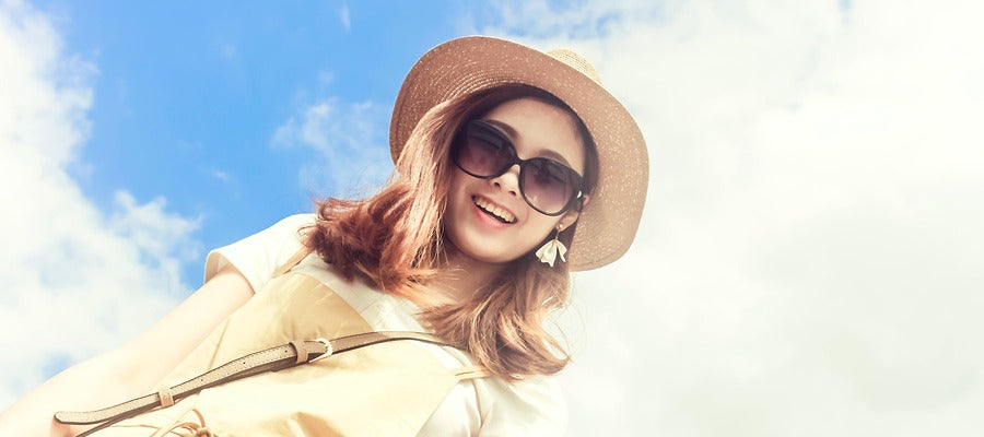 retrato de mujer con sombrero mirando hacia abajo y sonriendo contra el cielo azul nublado su rostro visto desde un ángulo inclinado