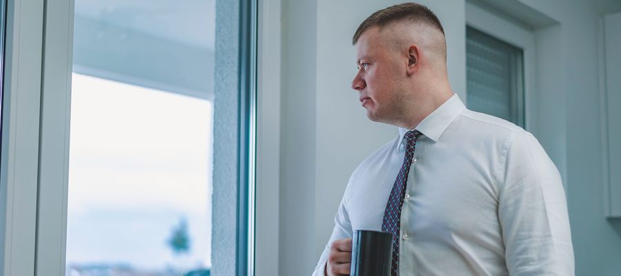 male office worker with coffee mug gazing out the window