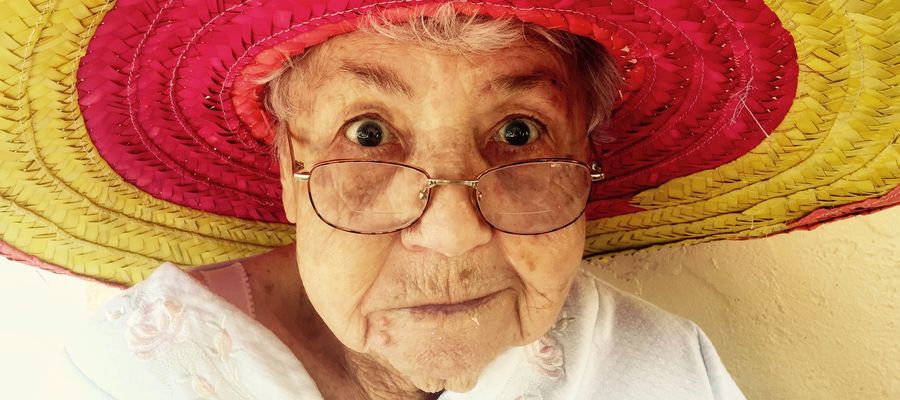 old woman with eyeglasses wearing a large hat looking at you with wide eyes