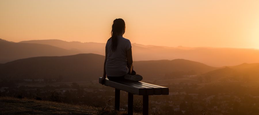woman sitting bench cross legged watching the landscape seen from behind