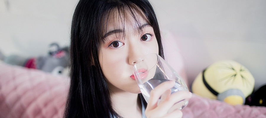 Mujer con cabello y ojos oscuros bebiendo agua de un vaso.