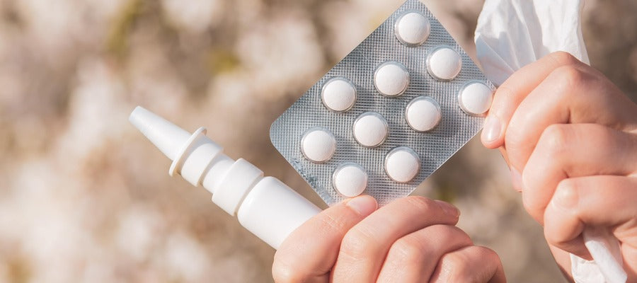 hands holding nasal decongestant, tablet of pills, and napkin against blurry nature background