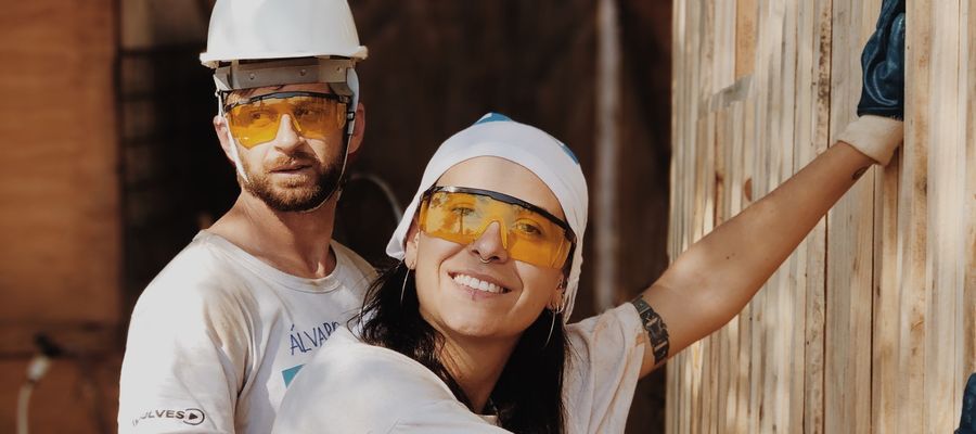 man and woman doing DIY project wearing yellow safety glasses and protective headwear
