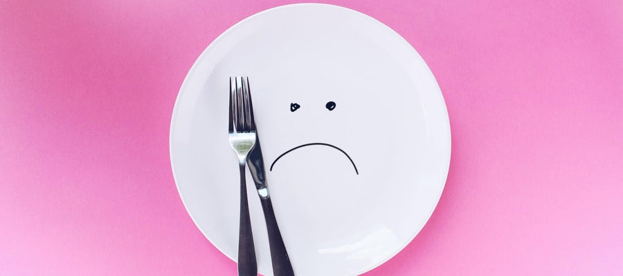 white plate with sad face drawn on it and fork and knife to one side