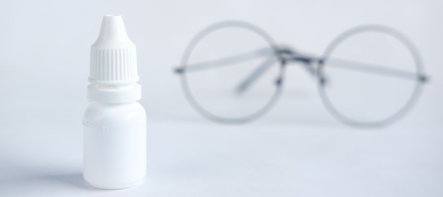 bottle of white eye drops without label with round glasses blurred in the background