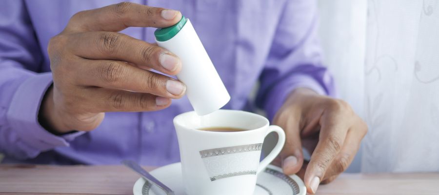 la mano del hombre poniendo un edulcorante apto para la diabetes en una taza de café mientras su otra mano sostiene el platillo