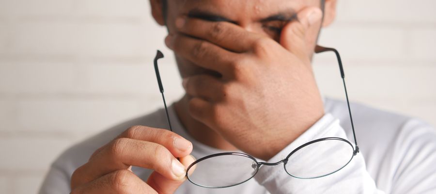 man taking off eyeglasses and rubbing eyes