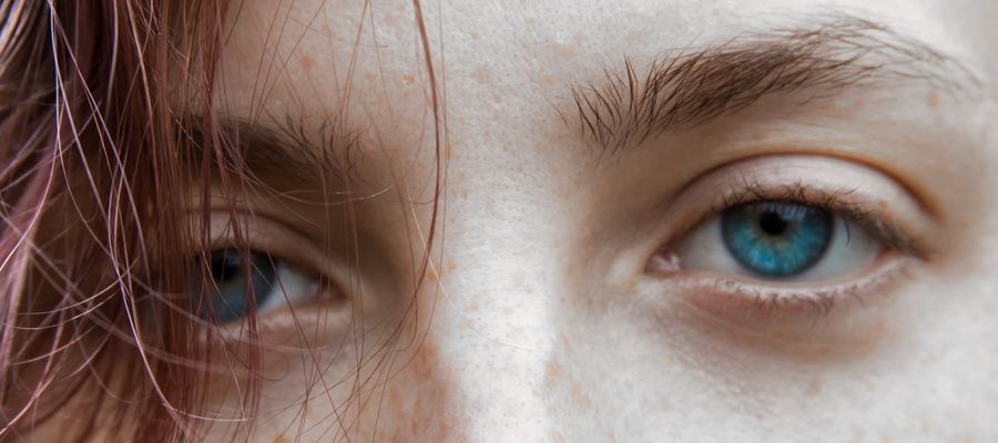 Primer plano de ojos femeninos azules con cabello cayendo sobre el ojo derecho.