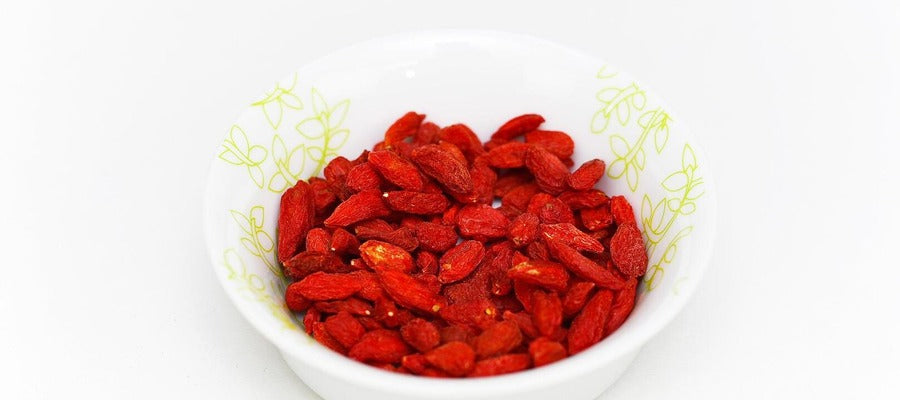 dried goji berries in small white bowl against white background