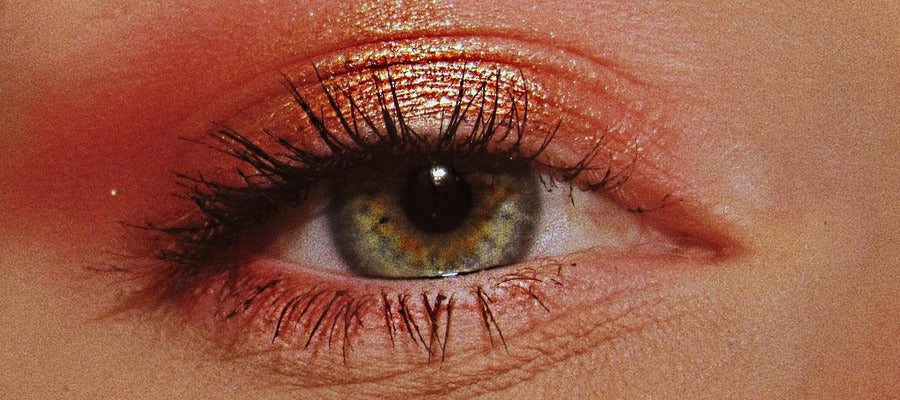 Primer plano de un ojo con rímel y maquillaje de sombra de ojos roja.