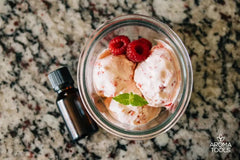 A serving of homemade raspberry ice cream with lime essential oil in a glass bowl and topped with fresh raspberries and a sprig of peppermint leaves.