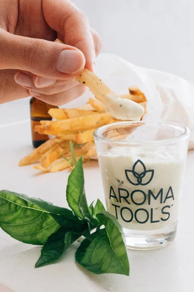 A close up view of the creamy basil dip in our AromaTools branded shot glass as a hand is dipping a fry into it.