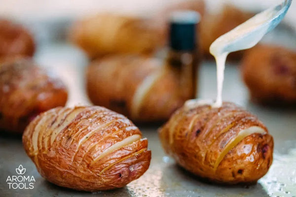 A spoon pouring on the essential oil herb butter onto freshly baked hasselback potatoes on a baking sheet.