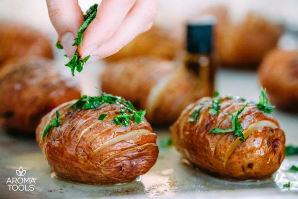 A close up of a hand adding fresh parsley bits to the baked hasselback potatoes on a baking sheet.