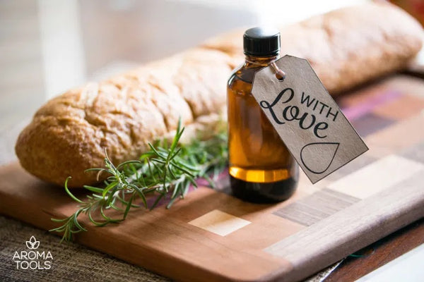 A 2 ounce glass jar filled with Italian dipping oil and has a gift tag tied to it sitting on a cutting board with a loaf of French bread.