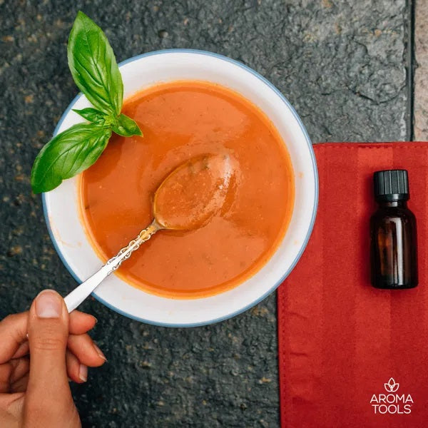 A bowl of homemade tomato basil soup made with basil and black pepper essential oils and a spring of basil leaves for decoration.