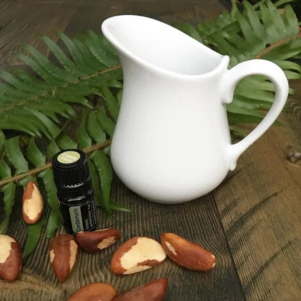 A small creamer pitcher filled with milk and a vial of cardamom essential oil and Brazilian nuts to the side.