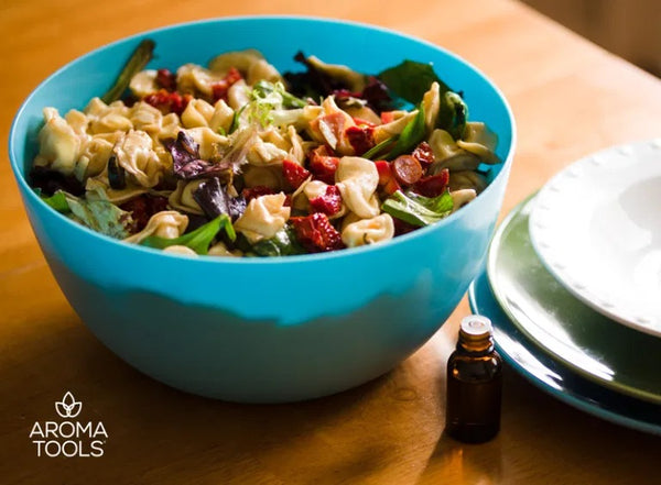 A serving bowl of cheese tortellini pasta with olives, arugula, peppers, and artichoke with a homemade dressing made with basil, lemon and oregano essential oils.