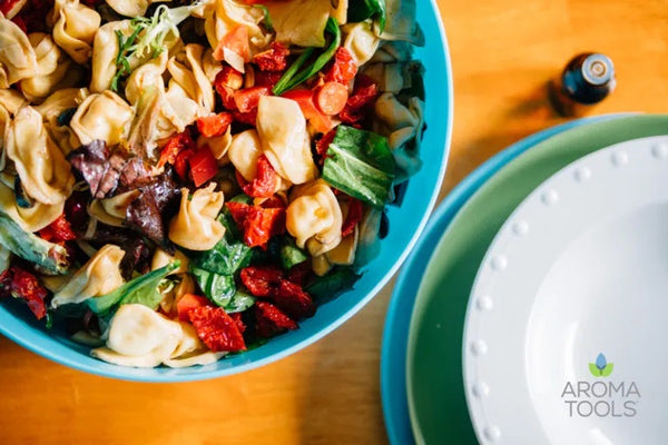 A serving bowl of cheese tortellini pasta with olives, arugula, peppers, and artichoke with a homemade dressing made with basil, lemon and oregano essential oils.
