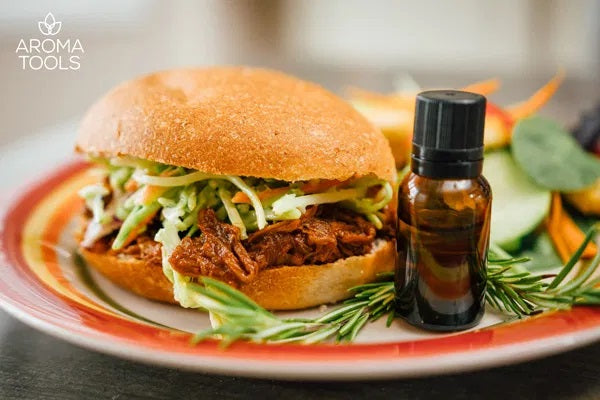 Our essential oil-flavored honey balsamic pulled pork and coleslaw in a fresh bun on a plate with a sprig of rosemary leaves.