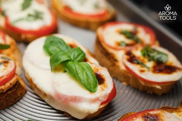 A close up of the toasted Margherita Garlic Bread with tomato slices and mozzarella cheese and a sprig for basil sitting on a baking sheet.