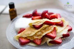 Homemade crepes filled with fresh strawberry slices and whipped cream flavored with lemon essential oil on glass plate.