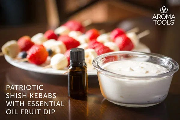 A generous serving of essential oil-flavored fruit dip in a glass bowl with strawberry, banana and blueberry kebobs in the background.