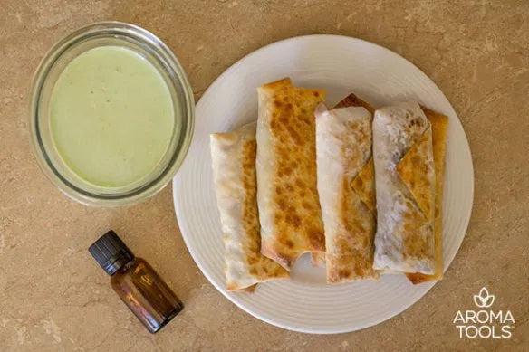 Four southwestern egg rolls flavored with black pepper essential oil stacked on a plate with a bowl of cilantro lime dipping sauce to the side.
