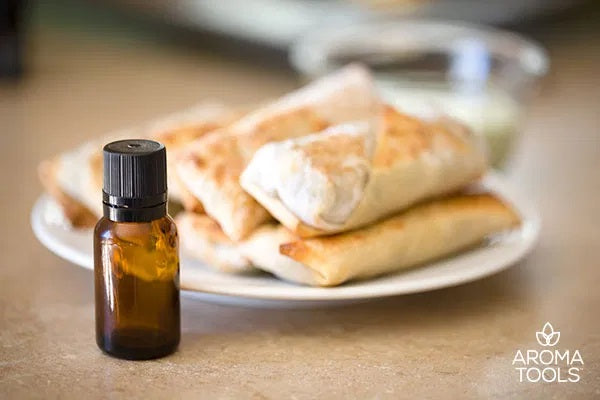 An essential oil vial with a stack of southwestern egg rolls flavored with black pepper essential oil on a plate with a bowl of cilantro lime dipping sauce in the back.