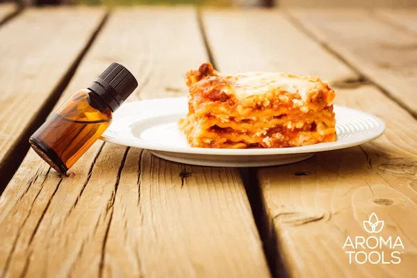 A plate with a generous slice of homemade lasagna sitting on a plate outside on wooden steps with an essential oil vial.