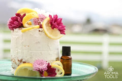 A small French yogurt cake with light lemon essential oil frosting decorated with flowers and lemon slices sitting on glass platter outside.