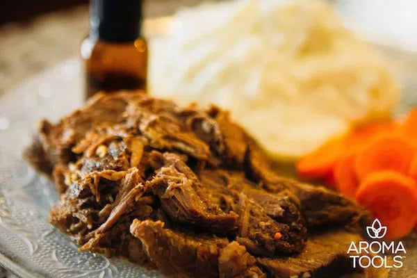 Our signature slow cooked pot roast seasoned with garlic and marjoram, rosemary and thyme essential oils with sides of cooked carrot slices and mashed potatoes on a glass plate.