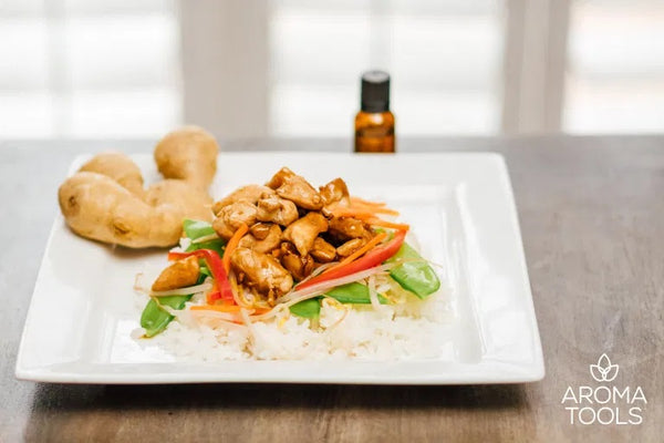 A plate of white rice with chicken and vegetables drizzled with homemade teriyaki sauce accented with a ginger root and an essential oil vial.