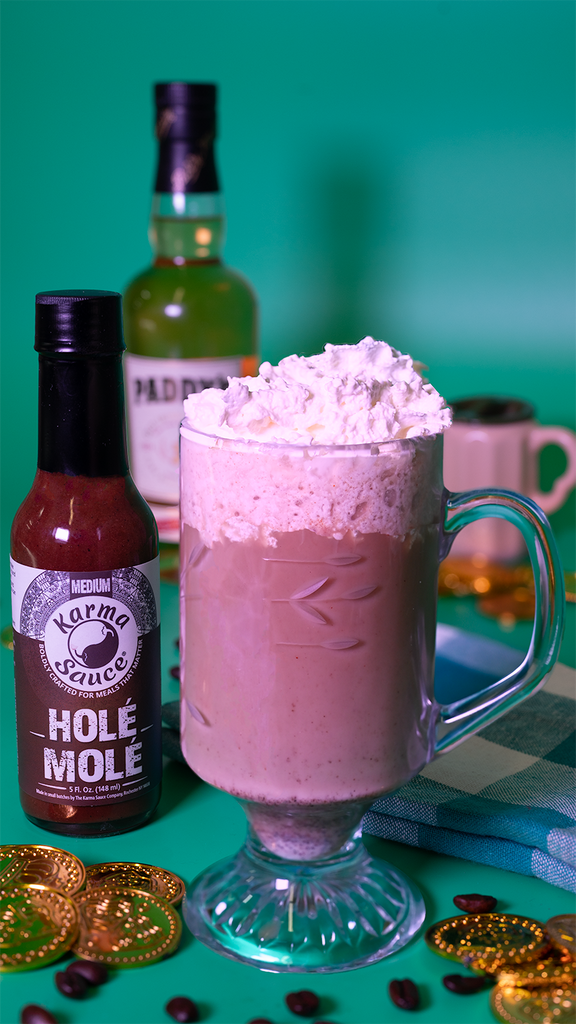 A mug of Irish Coffee next to Hole Mole Hot Sauce. Irish Whiskey, gold coins, and coffee beans are visible in the background and foreground.